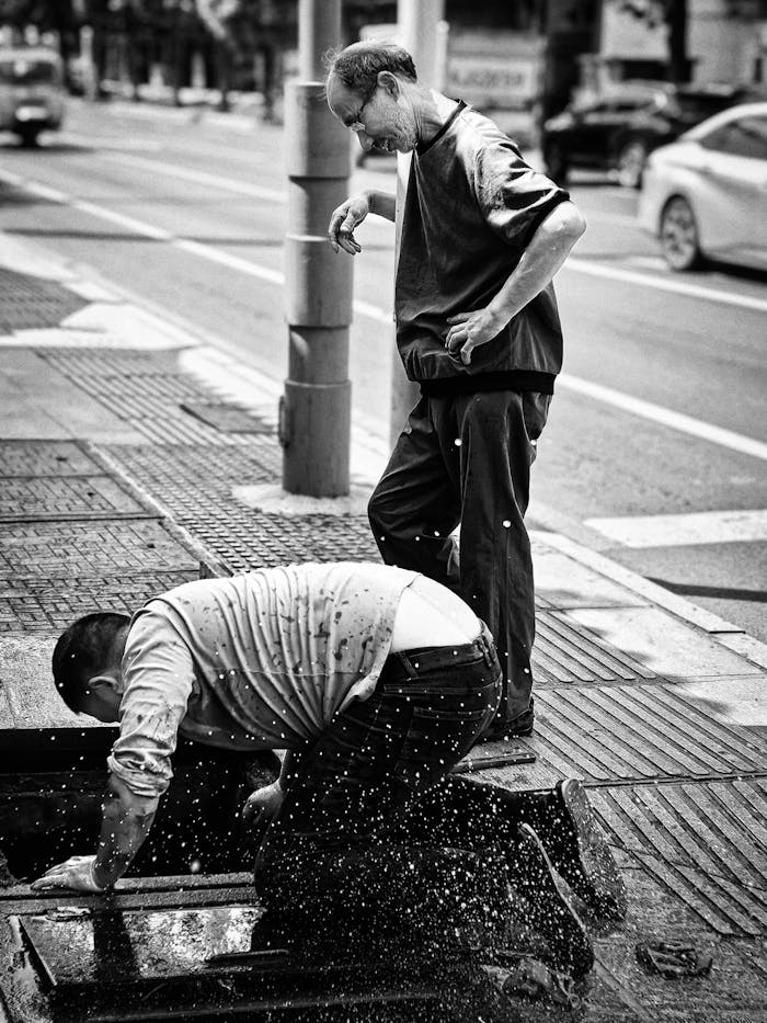 Two workers examining a street drain in Changde, Hunan Province, showcasing urban life and maintenance.